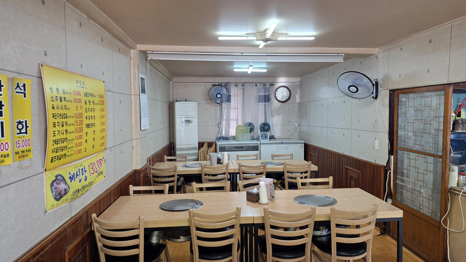 An indoor dining area with a wall menu, wooden chairs and tables, each with a round grilling brazier