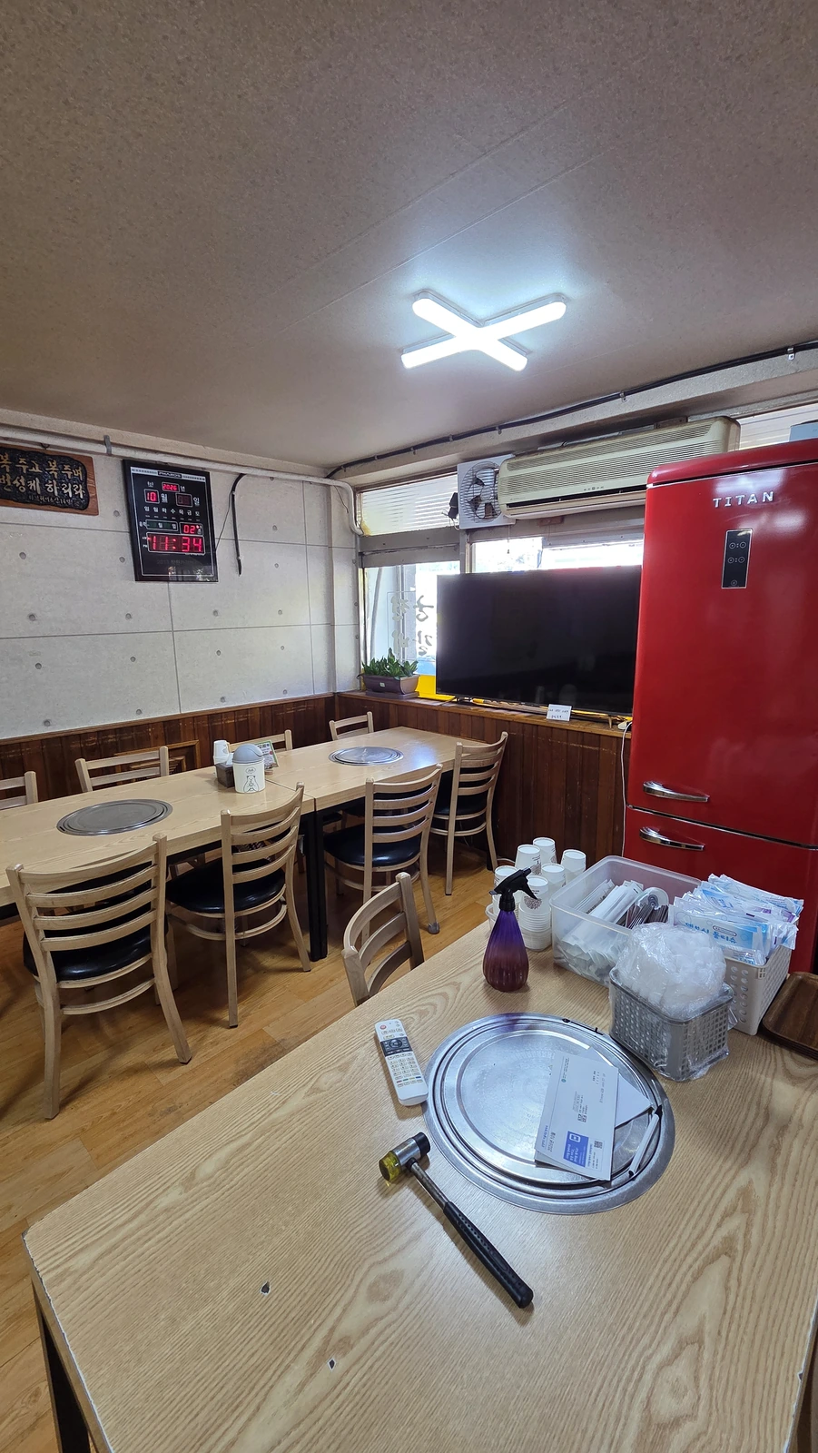 Wooden tables with round grilling braziers by the window, a television and a refrigerator
