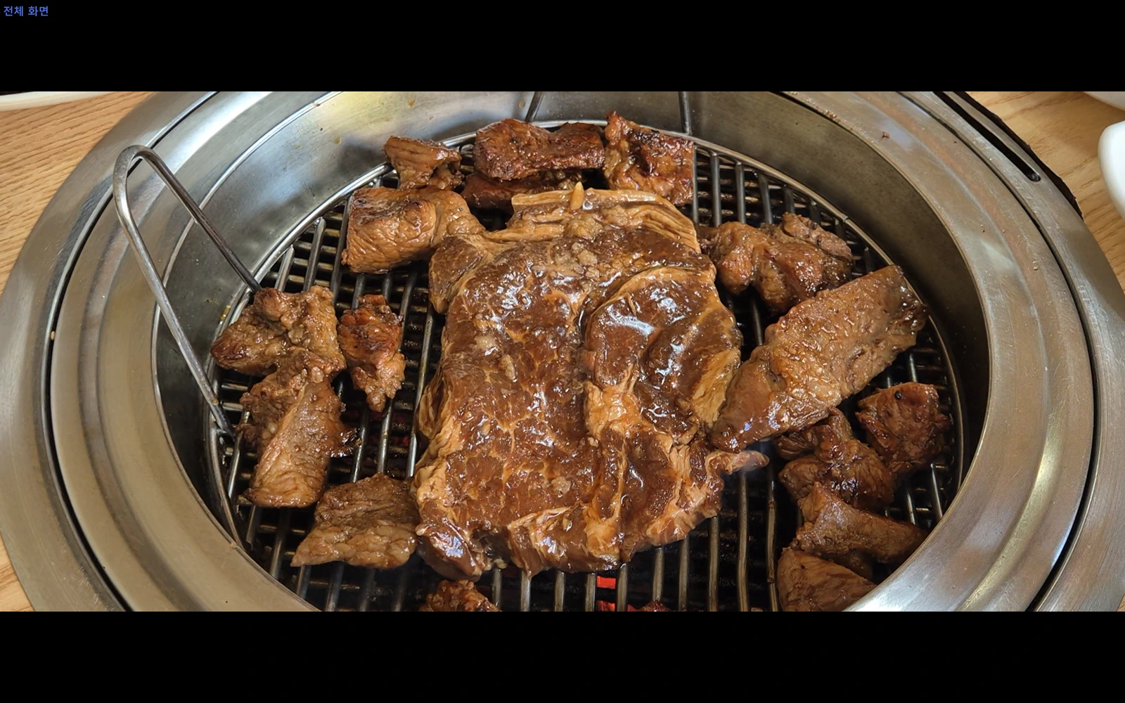 원형 화로의 구이망 위에 크게 펼친 갈비와 작은 고기 조각들이 놓여 있는 모습